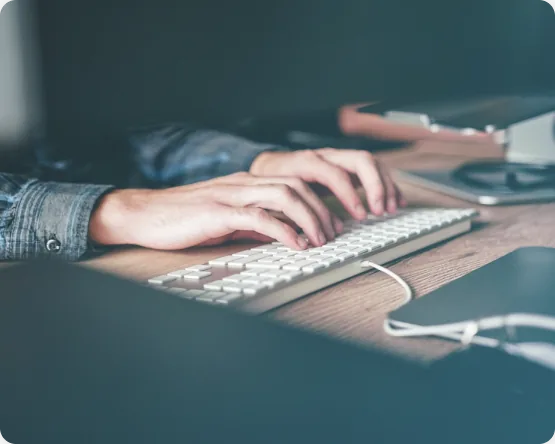 Close up of a person working at a desk, hands on a keyboard beside paperwork